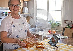 Happy senior woman shows a pan with homemade stuffed cannelloni ready for the oven. Ingredients around her