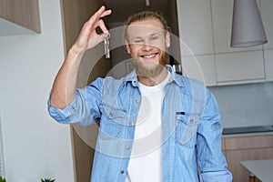 Smiling proud young man renter first time estate owner holding key to new home.