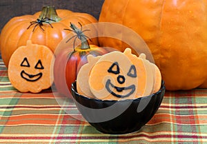 Smiling pumpkin shaped sugar cookies in a black bowl