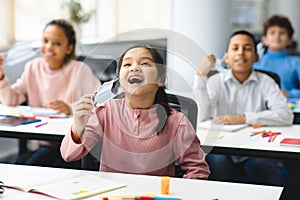 Smiling pupils taking off disposable medical face mask at classroom