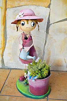 Smiling puppet made in colorful steel that shows a happy cross-eyed girl watering can a bucket with a green plant on a yellow