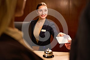 Smiling receptionist standing and giving keycard to hotel guest