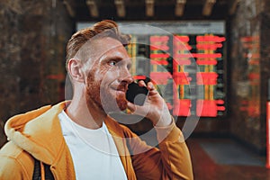 Smiling red haired man talking on cellphone while waiting for train