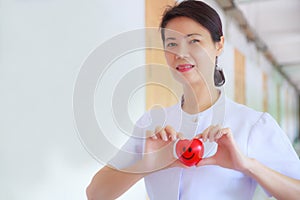 Smiling Red heart held by smiling female nurse`s hand in health care hospital or clinic. Professional, Specialist, Experienced