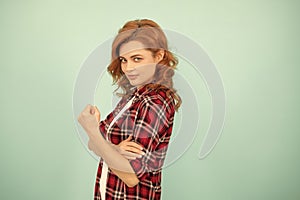 smiling redhead woman in checkered shirt threatening with fist on blue background