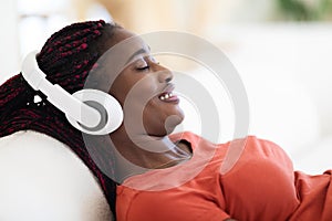 Smiling Relaxed Black Woman In Wireless Headphones Listening Music At Home