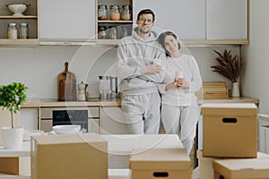 Smiling relaxed husband and wife drink coffee at kitchen, hold paper cups with hot beverage, dressed in casual outfit, relocate in