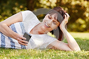 Smiling relaxed woman lying in grass with smart phone