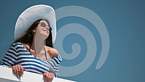 Smiling relaxed woman in trendy sunglasses and white hat enjoying vacation on balcony medium shot