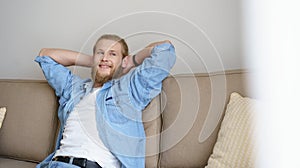 Smiling relaxed young man chill on comfortable couhc looking away.