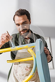 Smiling restorer painting on blurred chair