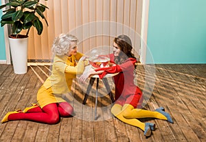 smiling retro styled women sitting on floor near golden fish in aquarium on coffee table doll