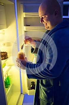 Smiling roly-poly guy at night take jar with jam from fridge