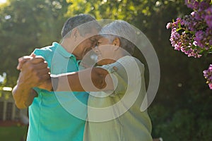 Smiling romantic biracial senior couple looking at each other while dancing against trees in park