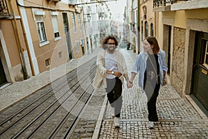 Smiling romantic hipster couple in love holding hands while walking on old city street in Lisbon