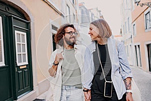 Smiling romantic hipster couple in love holding hands while walking on old city street in Lisbon