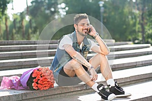 Smiling romantig guy speaking on the phone, bouquet of roses