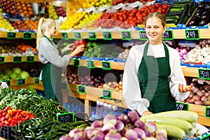 Smiling salesgirl offering fruits and vegetables in family shop