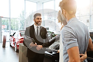 Smiling salesman showing new car to a couple