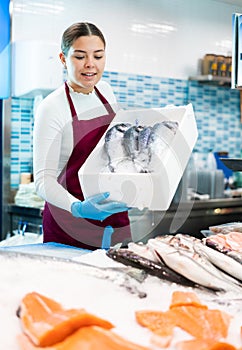 Smiling saleswoman holding dorada in fish store