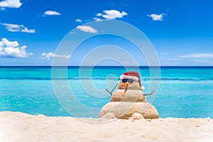 Smiling sandy snowman with red santa hat on the caribbean beach with beautiful sky . Holiday concept for New Year and Christmas