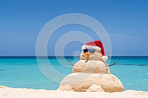 Smiling sandy snowman with red santa hat on the caribbean beach. Holiday concept for New Year and Christmas Cards photo