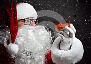 Smiling Santa Claus is holding red salmon caviar sandwich, looking glancing at us going to eat under the snow.