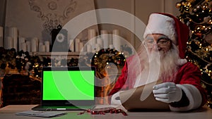 Smiling Santa Claus reading letter with list of gifts, laptop green screen