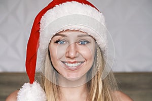 Smiling Santa girl wearing red hat looking at camera. Portrait of beautiful young blue-eyed blonde woman in Santa& x27;s