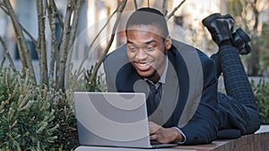 Smiling satisfied ethnic businessman corporate employee African American funny worker man lying down on bench work with