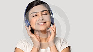 Smiling satisfied Indian girl in headphones enjoying favorite music