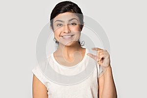 Smiling satisfied Indian girl showing little size gesture with fingers