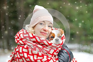 Smiling, satisfied woman in warm clothes, wrapped in red blanket with cavalier Charles king spaniel dog on winter walk