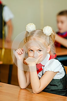 Smiling scholar girl sitting with other children in classroom and writing on textbook. Happy student doing homework at elementary