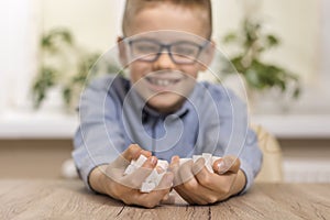 A smiling school-age boy sits at a table and puts a teaspoon of white sugar in his mouth.