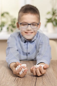 A smiling school-age boy sits at a table and puts a teaspoon of white sugar in his mouth.