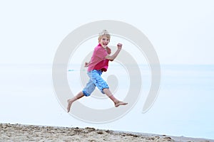 Smiling school boy jumping on the beach