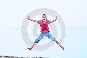 Smiling school boy jumping on the beach