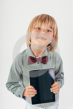 Smiling School boy in shirt with red bow tie, holding tablet computer and green apple in white background