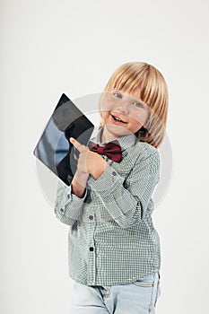 Smiling School boy in shirt with red bow tie, holding tablet computer and green apple in white background