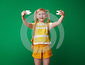 Smiling school girl showing puzzle pieces on green background