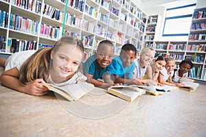 Smiling school kids lying on floor reading book in library