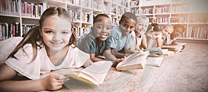 Smiling school kids lying on floor reading book in library