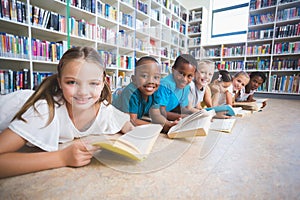 Smiling school kids lying on floor reading book in library