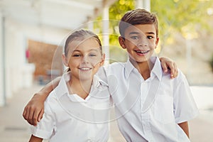 Smiling school kids standing with arm around in corridor