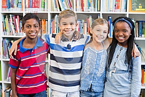 Smiling school kids standing with arm around in library