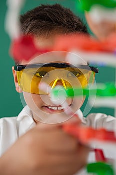 Smiling schoolboy experimenting molecule model in laboratory