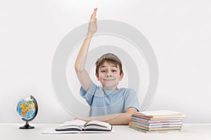 Smiling schoolboy raised his hand during the lesson. Excellent student knows the answer. Portrait of student at table next to