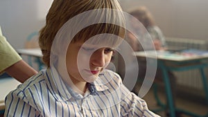 Smiling schoolboy siting at desk in school class. Male student looking down