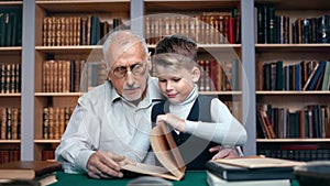 Smiling schooler boy bringing ancient retro book learning history science grandfather at library